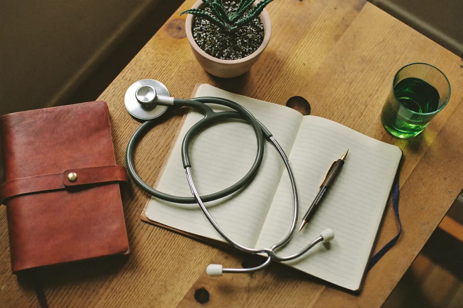 A doctor's desk in warm morning light — stethoscope, notebook and a glass of mint tea